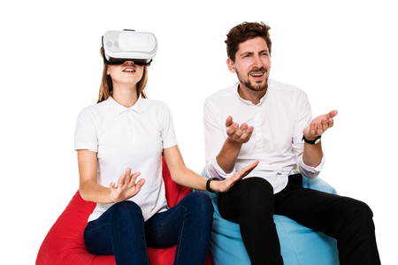Excited young couple experiencing virtual reality seated on beanbags isolated on white backgroundの写真素材