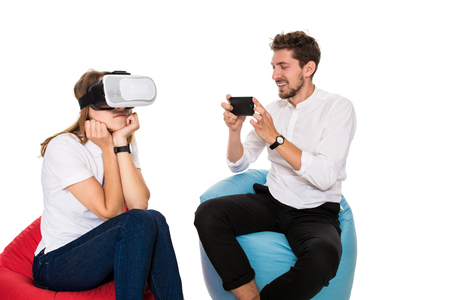 Excited young couple experiencing virtual reality seated on beanbags isolated on white backgroundの写真素材