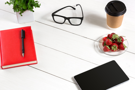 Office table desk with set of supplies, red notepad, cup, pen, tablet, glasses, flower on white background. Top viewの写真素材