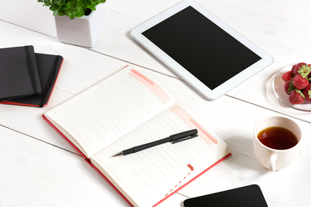 Office table desk with set of supplies, white blank notepad, cup, pen, tablet, flower on white background. Top viewの写真素材