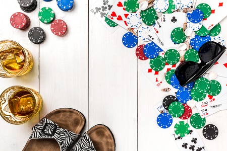 Card deck surrounded by poker chips and scattered seashells on white wooden background with copy spaceの写真素材