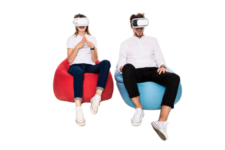 Excited young couple experiencing virtual reality seated on beanbags isolated on white backgroundの写真素材