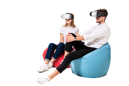 Excited young couple experiencing virtual reality seated on beanbags isolated on white backgroundの写真素材