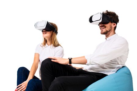 Excited young couple experiencing virtual reality seated on beanbags isolated on white backgroundの写真素材