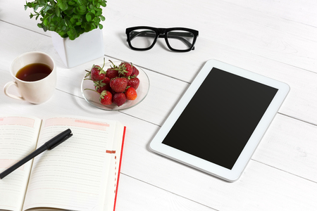 Office table desk with set of supplies, white blank notepad, cup, pen, tablet, glasses, flower on white background. Top viewの写真素材