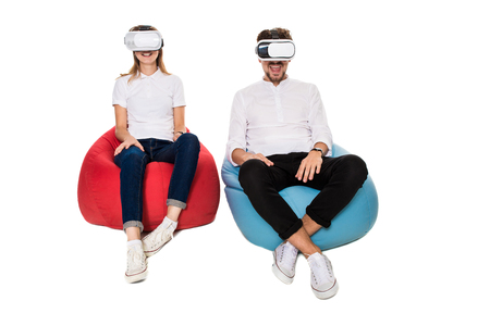 Excited young couple experiencing virtual reality seated on beanbags isolated on white backgroundの写真素材