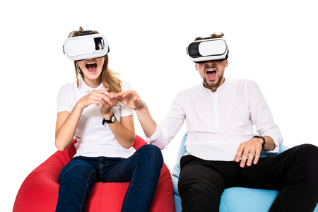 Excited young couple experiencing virtual reality seated on beanbags isolated on white backgroundの写真素材