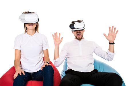 Excited young couple experiencing virtual reality seated on beanbags isolated on white backgroundの写真素材