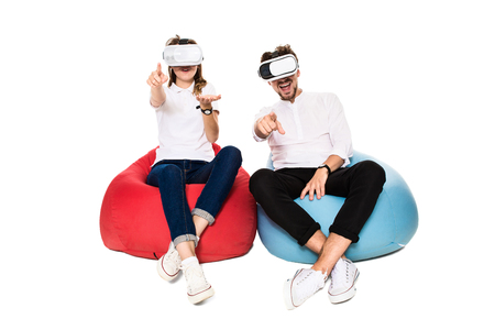 Excited young couple experiencing virtual reality seated on beanbags isolated on white backgroundの写真素材