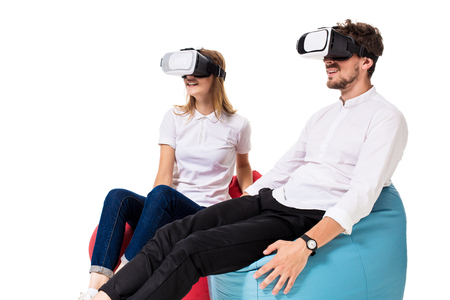 Excited young couple experiencing virtual reality seated on beanbags isolated on white backgroundの写真素材