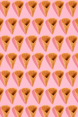 Sugar waffle cone for ice cream arranged in pattern on pink background. The image with copy space can be used as a background for the design of the confectionery menuの写真素材
