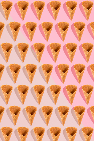 Sugar waffle cone for ice cream arranged in pattern on pink background. The image with copy space can be used as a background for the design of the confectionery menuの写真素材