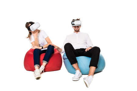 Excited young couple experiencing virtual reality seated on beanbags isolated on white backgroundの写真素材