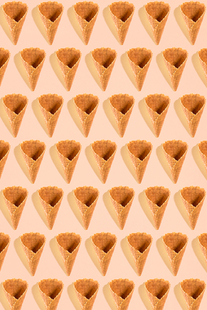 Sugar waffle cone for ice cream arranged in pattern on pink background. The image with copy space can be used as a background for the design of the confectionery menuの写真素材