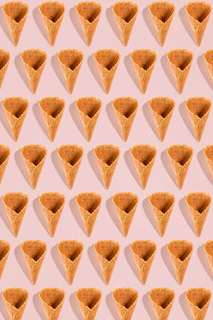 Sugar waffle cone for ice cream arranged in pattern on pink background. The image with copy space can be used as a background for the design of the confectionery menuの写真素材
