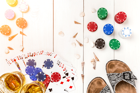 Card deck surrounded by poker chips and scattered seashells on white wooden background with copy spaceの写真素材