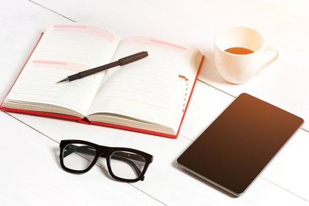 Office table desk with set of supplies, white blank notepad, cup, pen, tablet, glasses on white background. Top viewの写真素材