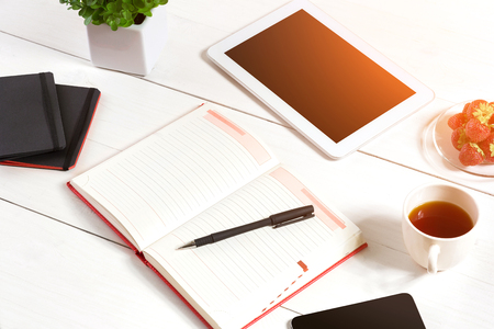 Office table desk with set of supplies, white blank notepad, cup, pen, tablet, flower on white background. Top view and copy space for text. sun flareの写真素材