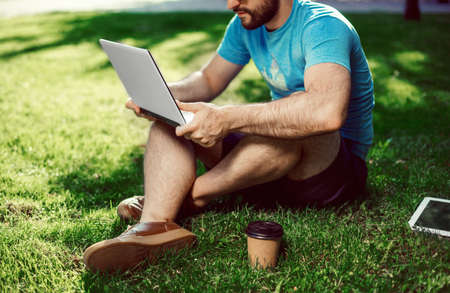 Young blogger sitting on grass and working with laptopの写真素材