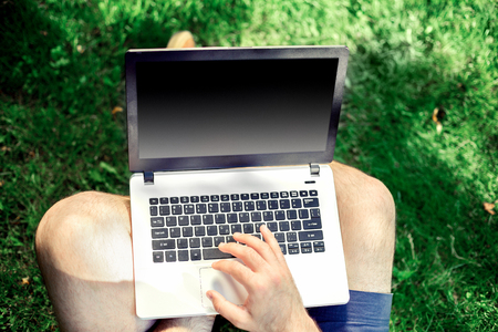 Young blogger sitting on grass and working with laptopの写真素材