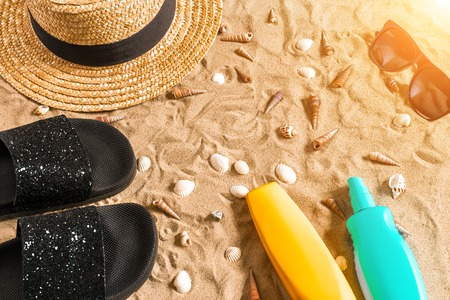 Summer beachwear, flip flops, hat, sunglasses and seashells on sand beach. Top view. Copy space. Sun flareの写真素材