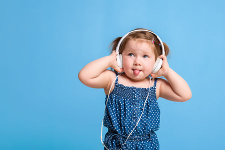 Cute little girl in headphones listening to music using a tablet and smiling on blue backgroundの写真素材