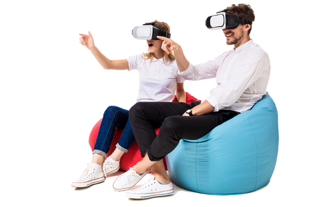 Excited young couple experiencing virtual reality seated on beanbags isolated on white backgroundの写真素材