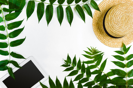 Green leaf branches, tablet and straw haton white background. flat lay, top view. Copy space. Still life.の写真素材