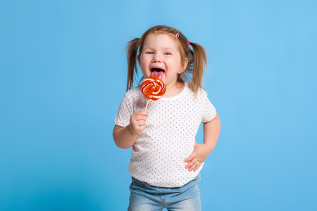 Beautiful little female child holding huge lollipop spiral candy smiling happy isolated on blue background.の写真素材