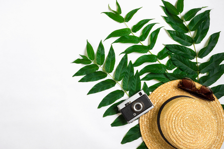 Straw hat with green leaves and old camera on white background, Summer background. Top view. Copy space. Still life. Flat layの写真素材