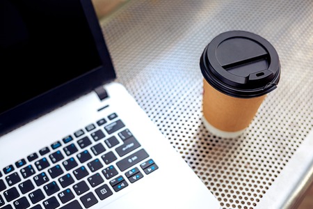 Mockup image of laptop with blank black screen and coffee cup on metal bench in nature outdoor park. Freelance work.の写真素材