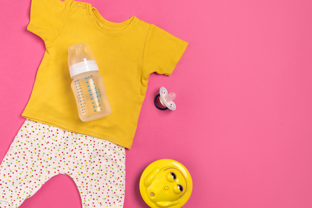 Yellow children's costume, bottle and orthodontic pacifier on a pink background. Top view. Copy space. Flat lay. Still lifeの写真素材