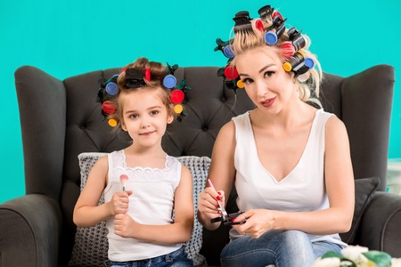 Mom and daughter in the studio on the sofa in the curlers make up and have funの写真素材