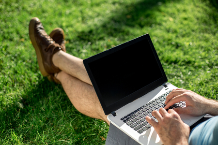 Cropped shot of man using laptop with blank screen while sitting on green grassの写真素材