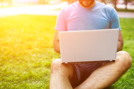 Young man using and typing laptop computer in summer grass.の写真素材