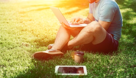 Young blogger sitting on grass and working with laptopの写真素材