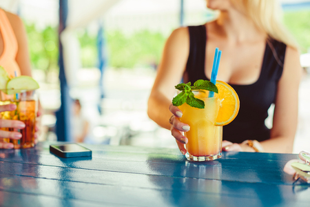 Cocktail in woman hand on the open terrace in bar during summer timeの写真素材