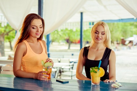 Two girls friends having fun outdoor in summer. Women with glasses of cocktail on vacationの写真素材
