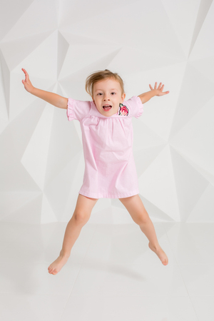 Photo of little girl jumping and raising hands against white backgroundの写真素材