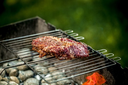 Hot spicy steak grilling on a summer barbecue over the hot coals garnished.