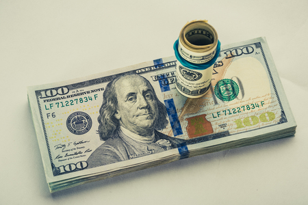A coiled 100 dollar bill which rests on another angled 100 dollar bill isolated on white background