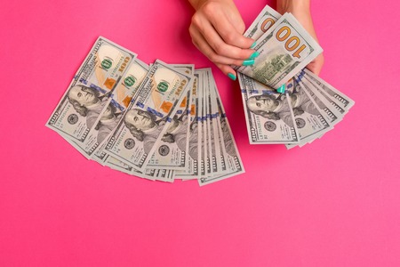 A woman is holding money in her hands. Pink background. Top view copy space.の写真素材