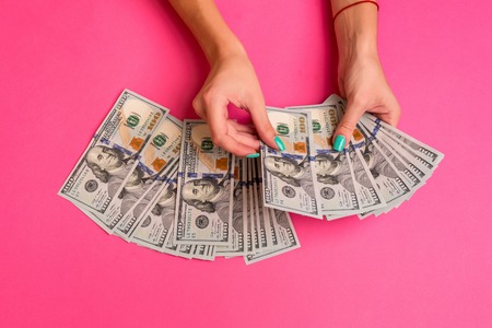 A woman is holding money in her hands. Pink background. Top view copy space.の写真素材