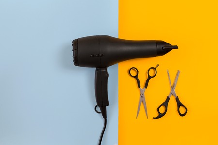Styling hair with scissors, dryer and tools in barbershop on blue and yellow paper background top...