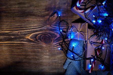 Fir tree branch with christmas lights, gift box and candy canes on wooden background with copy space.の写真素材