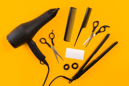 Black hair dryer, comb and scissors on yellow paper background. Top viewの写真素材