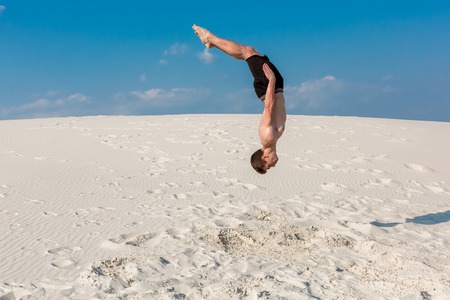 Portrait of young parkour man doing flip or somersault on the sand.の写真素材