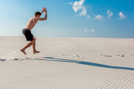 Young man jumping on the beach with white sand and bright blue skyの写真素材
