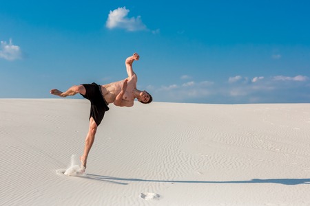 Portrait of young parkour man doing flip or somersault on the sand.の写真素材