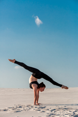 Young woman practicing handstand on beach with white sand and bright blue skyの写真素材